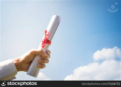 Hand holding Graduation certificate roll under the sunshine, blue sky background.