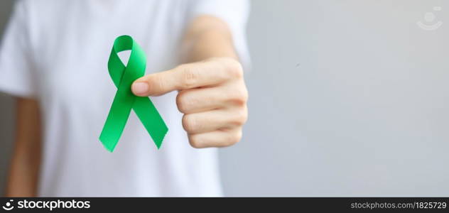 Hand holding green Ribbon for Liver, Gallbladders, bile duct, cervical, kidney Cancer and Lymphoma Awareness month. Healthcare and world cancer day concept