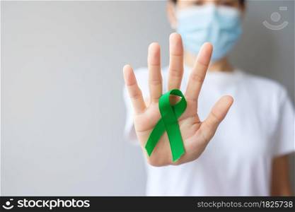 Hand holding green Ribbon for Liver, Gallbladders, bile duct, cervical, kidney Cancer and Lymphoma Awareness month. Healthcare and world cancer day concept