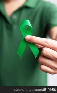 Hand holding green Ribbon for Liver, Gallbladders, bile duct, cervical, kidney Cancer and Lymphoma Awareness month. Healthcare and world cancer day concept