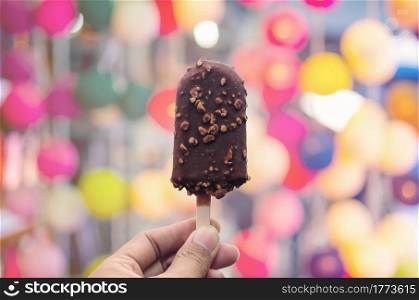 Hand holding Ice cream covered with chocolate on natural blurred background.. Hand holding Ice cream.