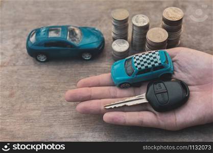 Hand holding Key of Car and Model coins stack on wooden table Finance insurance and Transportation concept