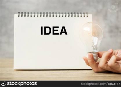 Hand holding lightbulb over notebook on table. New Ideas, Creative, Innovation, Imagination, inspiration, Resolution, Strategy and goal concept