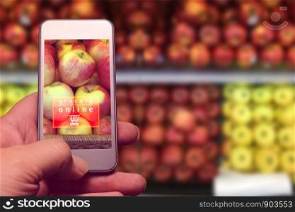 hand holding mobile with grocery online text with blur fruits in supermarket background