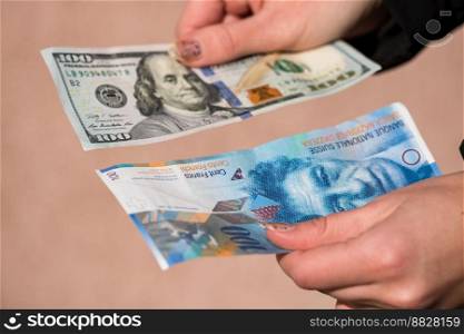 Hand holding money isolated on banknotes background. USD and CHF currency banknotes compared close up. Inflation, finance and business concept