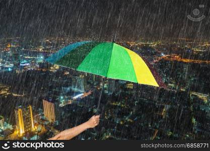 hand holding multicolored umbrella with falling rain at Bangkok city background, Thailand