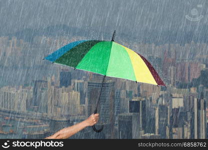 hand holding multicolored umbrella with falling rain at Hond Kong city background