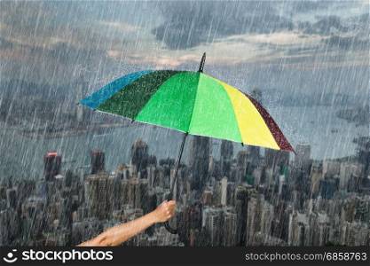 hand holding multicolored umbrella with falling rain at Hong Kong city background