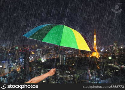 hand holding multicolored umbrella with falling rain at Tokyo city background, Japan
