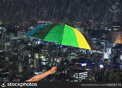hand holding multicolored umbrella with falling rain at Tokyo city background, Japan