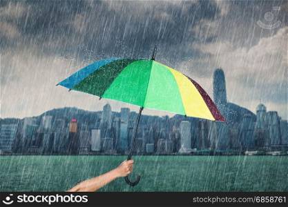 hand holding multicolored umbrella with falling rain at victoria harbour, Hong Kong