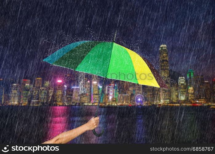 hand holding multicolored umbrella with falling rain at victoria harbour, Hong Kong