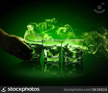 Hand holding one of three glasses of green absinth with fume going out