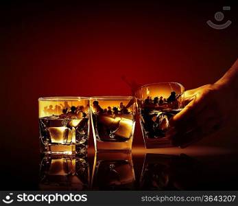 Hand holding one of three glasses of whiskey with ice and party illustration in