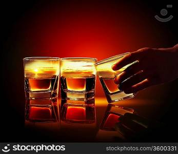 Hand holding one of three glasses of whiskey with sea illustration in