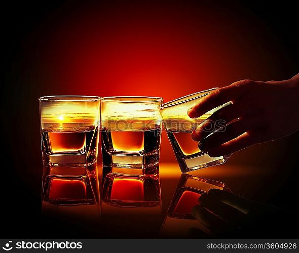 Hand holding one of three glasses of whiskey with sea illustration in