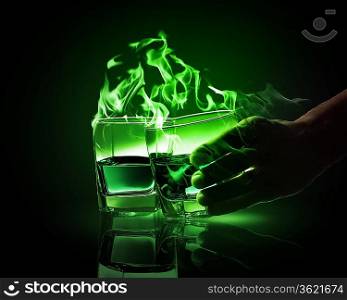 Hand holding one of two glasses of burning green absinth