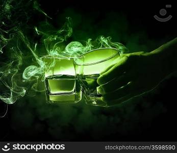 Hand holding one of two glasses of green absinth with fume going out