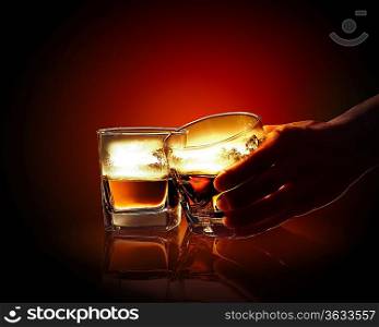 Hand holding one of two glasses of whiskey with nature illustration in