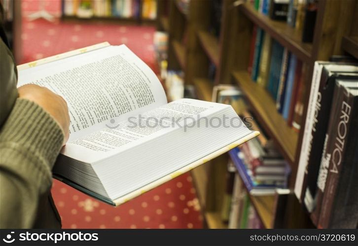 Hand holding open book in a bookstore. Many books on the background