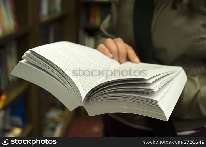 Hand holding open book in a bookstore. Many books on the background