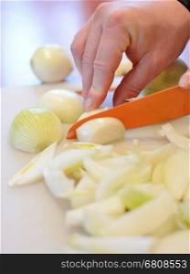 Hand holding orange ceramic knife and slicing the fresh onion into small pieces on cutting board.