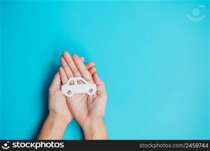 Hand holding paper Car cutout on blue background. Vehicle insurance, warranty, Automobile rental, Transportation, Maintenance and repair concept.