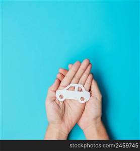 Hand holding paper Car cutout on blue background. Vehicle insurance, warranty, Automobile rental, Transportation, Maintenance and repair concept.