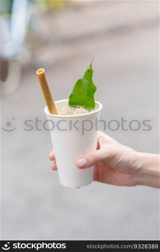 Hand holding paper cup of herbal drink with lotus petal and tea leaf, is the most popular beverage for tourists in Hoi An ancient town in central Vietnam