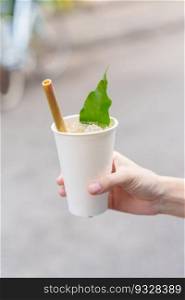 Hand holding paper cup of herbal drink with lotus petal and tea leaf, is the most popular beverage for tourists in Hoi An ancient town in central Vietnam