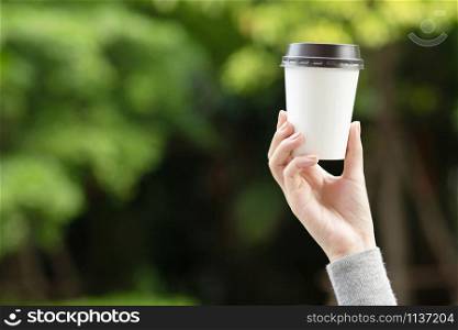 hand holding paper cup of take away drinking coffee on natural morning sunlight. space Place for your text or logo.