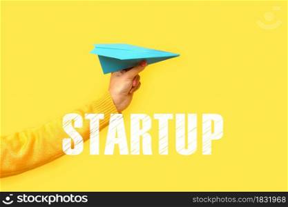 hand holding paper plane over yellow background, startup concept