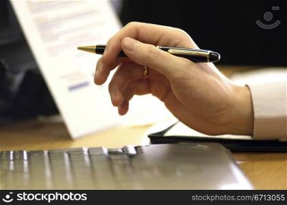 hand holding pen by laptop