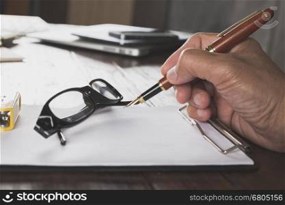hand holding pen with notepad and eyeglasses on wooden office desk