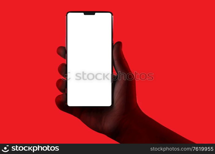 Hand holding phone. Silhouette of male hand holding smartphone isolated on red background. Bezel-less screen is cut with clipping path.. Hand holding phone.