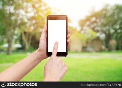 Hand holding phone with defocused bokeh and blur background of garden trees in sunlight.