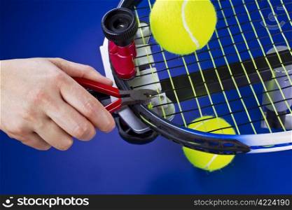 Hand holding pliers while trimming string on tennis racket on blue background