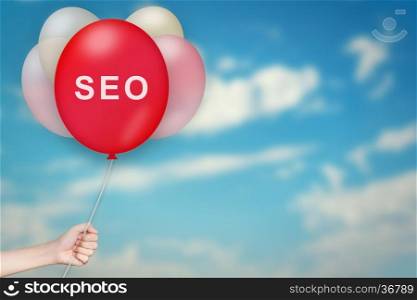 Hand Holding SEO or Search Engine Optimization Balloon with sky blurred background