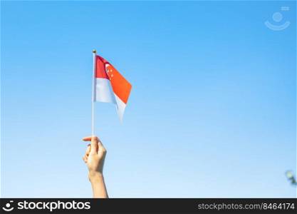 hand holding Singapore flag on blue sky background. Singapore National Day and happy celebration concepts