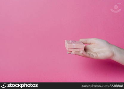 hand holding small gift box pink background