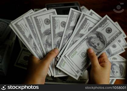 Hand holding smartphone and calculator on a stack of 100 US dollars banknotes lots of money