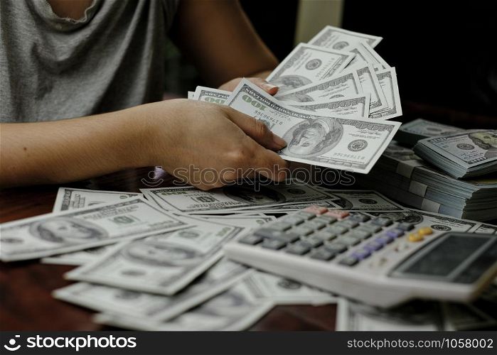 Hand holding smartphone and calculator on a stack of 100 US dollars banknotes lots of money