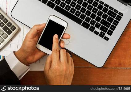 hand holding smartphone with laptop and office tools on wooden background in sunrise