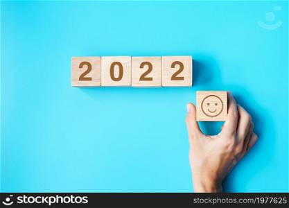 hand holding Smile face block with 2022 text on blue background. Satisfaction, feedback, Review and New Year concepts