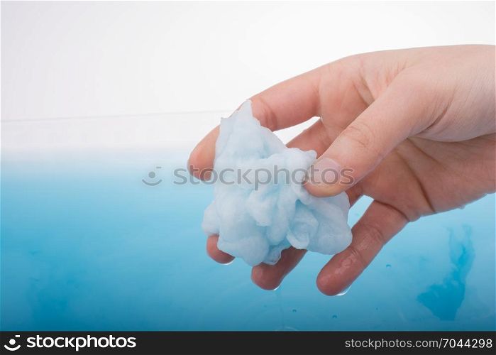 Hand holding some wet cotton over blue water