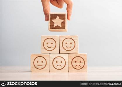 hand holding Star over emotion face symbol blocks on table background. Service rating, ranking, customer review, satisfaction, evaluation and feedback concept