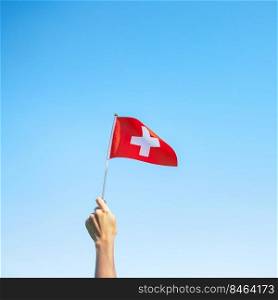 hand holding Switzerland flag on blue sky background. Switzerland National Day and happy celebration concepts