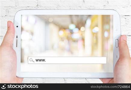 Hand holding tablet with www. on search bar over blur store background on screen, on line shopping ,business, E-commerce, technology and digital marketing background