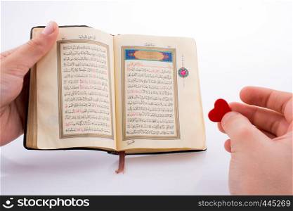 Hand holding The Holy Quran with a heart on a white background