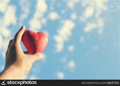 Hand holding the red decorative heart against the blue sky. Day of donor. Love concept. Toned photo. Hand holding the red decorative heart against the blue sky.